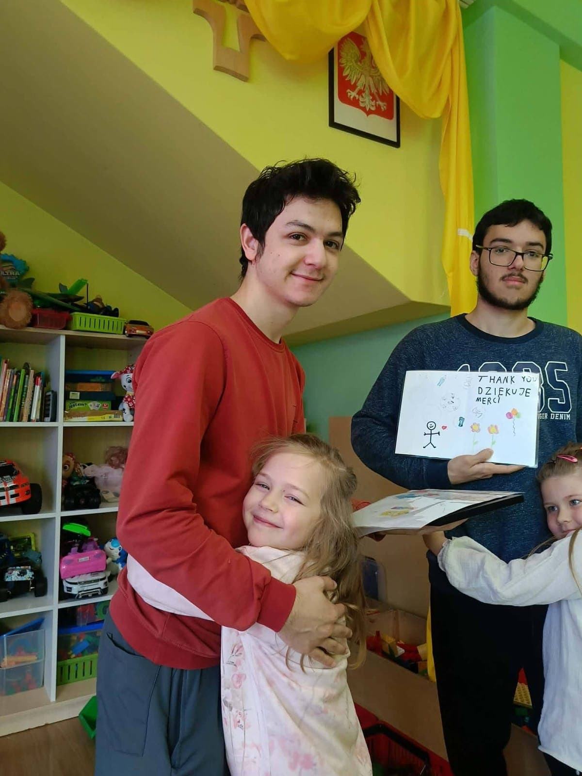 A child hugging an exchange participant while another holds up a drawing